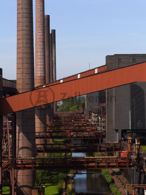 Die Kokerei Zollverein wurde von 1957 bis 1961 nach Plänen des Architekten Fritz Schupp gebaut, nach Erweiterungsarbeiten war sie ab 1973 die größte Zentralkokerei Europas. Täglich waren bis zu 1.000 Koker rund um die Uhr im Einsatz, bis zu 8.600 Tonnen Koks wurden pro Tag produziert. 1993 wurde die Kokerei stillgelegt. 2000 wurde die Kokerei in die Denkmalliste der Stadt Essen aufgenommen und gehört seit 2001 zum UNESCO-Welterbe. 2010 ist die Kokerei in den Besitz der Stiftung Zollverein übergegangen. Die „schwarze Seite“ der Kokerei, die den Bereich der Koksproduktion bezeichnet, kann bei einer Führung durch den Denkmalpfad ZOLLVEREIN® besichtigt werden.

Das große Wasserbecken des Druckmaschinengleises verwandelt sich im Winter in die 150 Meter lange ZOLLVEREIN® Eisbahn, die zum Freizeitvergnügen in faszinierender Atmosphäre einlädt. Früher wurde das Gleis von den Druckmaschinen befahren, sie hielten an jedem der 304 Koksöfen, öffneten sie und drückten den fertigen Koks heraus. Seit 1999 wird die Kokerei Zollverein mit „Monochromatic Red and Blue“ (1999) von Jonathan Speirs und Mark Major allabendlich zu einem riesigen Lichtkunstwerk.

Die Bandbrücken sind Teil des Gebäudeensembles der Kokerei Zollverein. Sie bilden die funktionale Verknüpfung zwischen den einzelnen Gebäuden und Anlageteilen auf der sogenannten „schwarzen“ Seite und verdeutlichen, welchen Weg die Kohle bzw. der Koks von der Zeche bis zur Verladung durchlaufen hat.

Ort: Areal C [Kokerei]