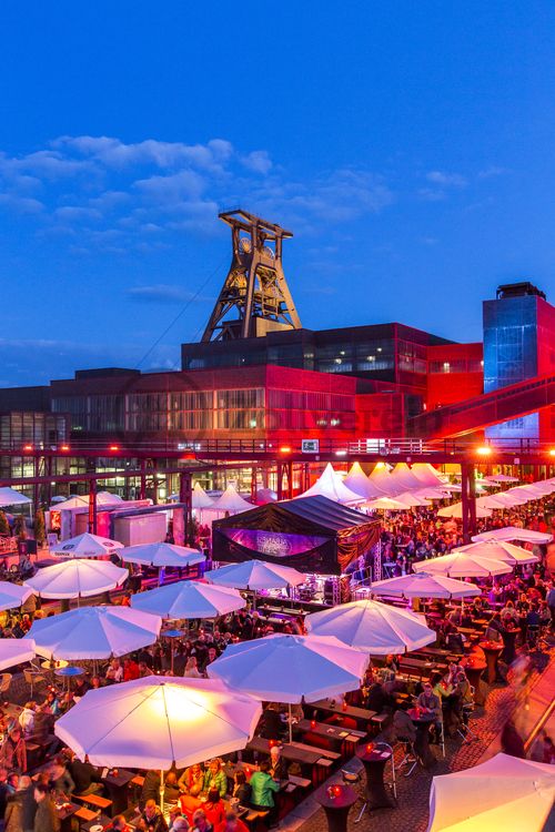 Einmal im Jahr treffen die regionalen Spitzengastronomen zur Gourmet-Meile Metropole Ruhr auf dem ehemaligen Gleisboulevard auf dem UNESCO-Welterbe Zollverein zusammen. Neben einer breiten Vielfalt kulinarischer Verlockungen bietet dieses Event ein anregendes und stimmungsvolles Ambiente für Gäste und Feinschmecker aus der ganzen Region.

Gleisboulevard nennt sich der Platz nördlich der Kohlenwäsche [A14] zwischen der Fritz-Schupp-Allee und der Halle 12 [A12]. Zu Betriebszeiten reihten sich dort die Waggons aneinander, die unter den Produktionsanlagen mit Kohle bzw. Bergematerial beladen wurden. 

Ort: Areal A [Schacht XII]

Das 55 Meter hohe Doppelbock-Fördergerüst ist das Wahrzeichen der Zeche Zollverein, der Stadt Essen und der gesamten Region: Die als Doppelstrebengerüst in Vollwandbauweise konstruierte Förderanlage ermöglichte eine doppelte Fördermechanik, mittels derer die doppelte Menge Förderwagen bzw. Fördergefäße transportiert werden konnten. Zollverein Schacht XII galt zu Betriebszeiten als die leistungsstärkste Zeche der Welt. 250 Stufen führen auf die oberste Plattform des Gerüstes, deren Seilscheiben sich auch heute noch drehen: Der Schacht wird heute von der RAG AG für die zentrale Wasserhaltung genutzt.

Pause machen im Bistro „Butterzeit!“ und Kunsthandwerk entdecken, wo früher Waggons mit Kohle beladen wurden: Die Ateliers im Erdgeschoss der Halle 12 [A12], darunter SchmuckProdukt und die ARKA Kulturwerkstatt, präsentieren neben eigenen Arbeiten auch wechselnde Ausstellungen anderer Künstler. Im Obergeschoss der ehemaligen Lesebandhalle finden heute Kongresse, Messen und Konzerte statt. Bis in die 1960er Jahre lasen hier Bergleute an fünf Lesebändern von Hand die großen Gesteinsstücke aus dem Rohkohlegemisch.

Der Wagenumlauf [A18] befindet sich zwischen der Wipperhalle und der Rückseite des Doppelbock-Fördergerüstes [A1]. In dem langgestreckten Gebäude wurden die Förderwagen, nachdem sie entleert wurden, wieder zurück zum Schacht geführt. Heute ist der Wagenumlauf Teil des Denkmalpfads ZOLLVEREIN®.