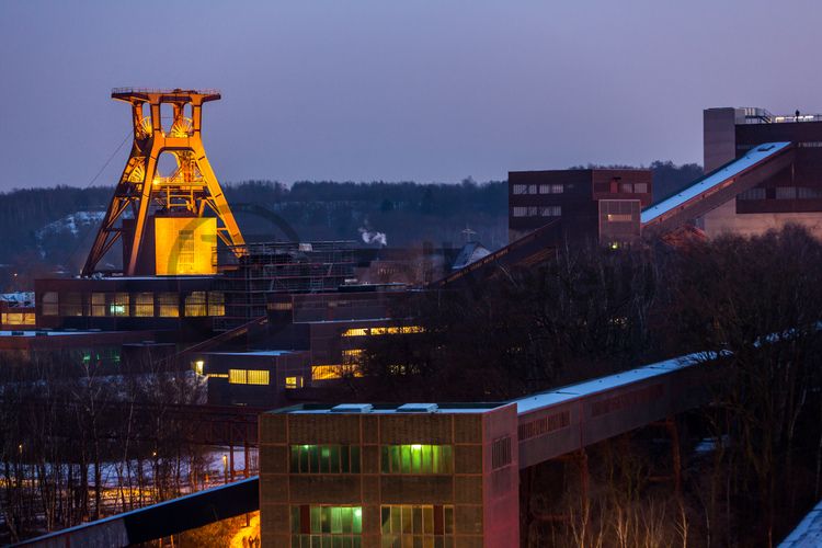 Die Geschichte Zollvereins beginnt in den Pioniertagen des heutigen Ruhrgebiets. Der erste Schacht wurde 1847 abgeteuft, d.h. in die Erde getrieben. Vier Jahre später wurde die erste Kohle gefördert. Im Laufe der Zeit entstanden vier weitere Schachtanlagen. Die letzte war die neue Zentralschachtanlage Zollverein XII, die ab 1932 die gesamte Zollverein-Kohle förderte. 

Noch heute besticht die symmetrische Anordnung der Gebäude auf zwei Blickachsen. Die komplett erhaltenen 20 Einzelgebäude bilden die technischen Arbeits- und Produktionsabläufe nach dem Prinzip „form follows function“ ab. Durchgestaltet bis in die Details der Lampen, Treppengeländer und Türgriffe, ist die Anlage ein komplett erhaltenes Gesamtkunstwerk. Die authentisch erhaltenen Anlagen repräsentieren exemplarisch die soziale, ökonomische, ästhetische und industrielle Geschichte des Kohle- und Stahlzeitalters. 

Trotz Rekordzahlen wie 12.000 Tagestonnen verwertbarer Steinkohle machte das Ende der Schwerindustrie auch vor Zollverein nicht Halt. Am 23. Dezember 1986 fuhr die letzte Schicht ein. An diesem Tag stand die Zeche bereits unter Denkmalschutz, 1990 begannen die Sanierungsarbeiten, seit 2001 sind Zeche und Kokerei Zollverein UNESCO-Welterbe. Mit dem Denkmalpfad ZOLLVEREIN®, dem Ruhr Museum und dem Red Dot Design Museum sind auf Schacht XII drei der beliebtesten Touristenziele der Region. Das Doppelbock-Fördergerüst der Schachtanlage ist heute Wahrzeichen für das gesamte Ruhrgebiet. 

Das 55 Meter hohe Doppelbock-Fördergerüst ist das Wahrzeichen der Zeche Zollverein, der Stadt Essen und der gesamten Region: Die als Doppelstrebengerüst in Vollwandbauweise konstruierte Förderanlage ermöglichte eine doppelte Fördermechanik. Dadurch konnte die doppelte Menge an Förderwagen bzw. Fördergefäßen transportiert werden. Zollverein Schacht XII galt zu Betriebszeiten als die leistungsstärkste Zeche der Welt. 250 Stufen führen auf die oberste Plattform des Gerüstes, deren Seilscheiben sich auch heute noch manchmal drehen: Der Schacht wird von der RAG AG für die zentrale Wasserhaltung genutzt.

Die diagonal und waagerecht zwischen den Gebäuden verlaufenden Bandbrücken sind fester Bestandteil der Gebäudeensembles von Zeche und Kokerei Zollverein. In ihrem Inneren befinden sich Bänder, auf denen die Rohkohle bzw. Kokskohle oder Koks zu den einzelnen Verarbeitungsstationen transportiert wurden. 

Das größte Übertagegebäude auf Zollverein, die Kohlenwäsche [A14], war zu Betriebszeiten eine Riesenmaschine: Täglich wurden dort 23.000 Tonnen Rohkohle sortiert und klassiert. Von 2003 bis 2006 wurde die Kohlenwäsche vom Office for Metropolitan Architecture (OMA) unter Leitung von Rem Koolhaas und dem Essener Büro Böll & Krabel umfassend saniert und für die spätere Nutzung vorbereitet. 

Eine 58 Meter lange Rolltreppe bringt die Besucher heute direkt in das RUHR.VISITORCENTER Essen auf der 24-Meter-Ebene. 2010 eröffnete das Ruhr Museum in der Kohlenwäsche, das in drei Etagen eine Dauerausstellung zu den Kategorien Gegenwart – Gedächtnis – Geschichte präsentiert. Die oberen Etagen gehören mit den authentisch erhaltenen Übertageanlagen zum Denkmalpfad ZOLLVEREIN®. Auf dem Dach der Kohlenwäsche sind zwei Aussichtsplattformen installiert, die einen Rundblick auf das Gelände und die Region bieten. Das Portal der Industriekultur informiert über industriekulturelle Angebote im Ruhrgebiet und in Nordrhein-Westfalen.

Areal A [Schacht XII]