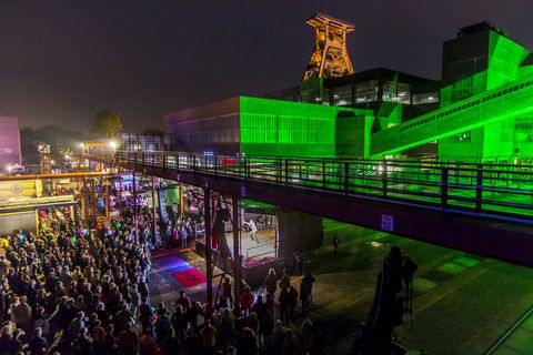 Seit der ersten ExtraSchicht im Jahr 2001 richtet die „Nacht der Industriekultur“ alljährlich ihr Rampenlicht auf die aktuellen und ehemaligen Stätten industrieller Arbeit im Ruhrgebiet. Das UNESCO-Welterbe Zollverein ist seit der ersten Stunde ein wichtiger Spielort für das Veranstaltungshighlight. Die Besucher auf Zollverein erwartet zwischen 18 Uhr und 2 Uhr nachts ein bunter Veranstaltungsmix mit vielen interaktiven Kulturangeboten, Ausstellungen, Musikbeiträgen, Licht- und Kunstinstallationen, Walk Acts und internationalen Straßentheaterinszenierungen. 

Das 55 Meter hohe Doppelbock-Fördergerüst ist das Wahrzeichen der Zeche Zollverein, der Stadt Essen und der gesamten Region: Die als Doppelstrebengerüst in Vollwandbauweise konstruierte Förderanlage ermöglichte eine doppelte Fördermechanik. Dadurch konnte die doppelte Menge an Förderwagen bzw. Fördergefäßen transportiert werden. Zollverein Schacht XII galt zu Betriebszeiten als die leistungsstärkste Zeche der Welt. 250 Stufen führen auf die oberste Plattform des Gerüstes, deren Seilscheiben sich auch heute noch manchmal drehen: Der Schacht wird von der RAG AG für die zentrale Wasserhaltung genutzt.

Areal A [Schacht XII], Fördergerüst [A1]

Zu Betriebszeiten wurde in der Lesebandhalle das taube Gestein von der Rohkohle von Hand getrennt. Bis in die 1960er Jahre lasen Bergleute an fünf Lesebändern von Hand die großen Gesteinsstücke aus dem zu Tage geförderten Rohkohlegemisch.
Im Obergeschoss der ehemaligen Lesebandhalle finden heute Kongresse, Messen und Konzerte statt. 

Die Halle 12 kann für Veranstaltungen angemietet werden. Kontakt: Stiftung Zollverein, Fon +49 201 246 81-355, locations@zollverein.de.

Areal A [Schacht XII], Halle 12 [A12]