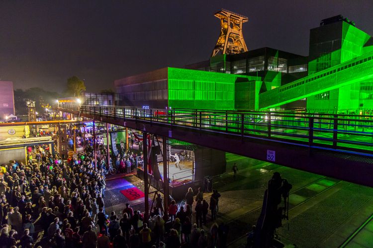 Seit der ersten ExtraSchicht im Jahr 2001 richtet die „Nacht der Industriekultur“ alljährlich ihr Rampenlicht auf die aktuellen und ehemaligen Stätten industrieller Arbeit im Ruhrgebiet. Das UNESCO-Welterbe Zollverein ist seit der ersten Stunde ein wichtiger Spielort für das Veranstaltungshighlight. Die Besucher auf Zollverein erwartet zwischen 18 Uhr und 2 Uhr nachts ein bunter Veranstaltungsmix mit vielen interaktiven Kulturangeboten, Ausstellungen, Musikbeiträgen, Licht- und Kunstinstallationen, Walk Acts und internationalen Straßentheaterinszenierungen. 

Das 55 Meter hohe Doppelbock-Fördergerüst ist das Wahrzeichen der Zeche Zollverein, der Stadt Essen und der gesamten Region: Die als Doppelstrebengerüst in Vollwandbauweise konstruierte Förderanlage ermöglichte eine doppelte Fördermechanik. Dadurch konnte die doppelte Menge an Förderwagen bzw. Fördergefäßen transportiert werden. Zollverein Schacht XII galt zu Betriebszeiten als die leistungsstärkste Zeche der Welt. 250 Stufen führen auf die oberste Plattform des Gerüstes, deren Seilscheiben sich auch heute noch manchmal drehen: Der Schacht wird von der RAG AG für die zentrale Wasserhaltung genutzt.

Areal A [Schacht XII], Fördergerüst [A1]

Zu Betriebszeiten wurde in der Lesebandhalle das taube Gestein von der Rohkohle von Hand getrennt. Bis in die 1960er Jahre lasen Bergleute an fünf Lesebändern von Hand die großen Gesteinsstücke aus dem zu Tage geförderten Rohkohlegemisch.
Im Obergeschoss der ehemaligen Lesebandhalle finden heute Kongresse, Messen und Konzerte statt. 

Die Halle 12 kann für Veranstaltungen angemietet werden. Kontakt: Stiftung Zollverein, Fon +49 201 246 81-355, locations@zollverein.de.

Areal A [Schacht XII], Halle 12 [A12]