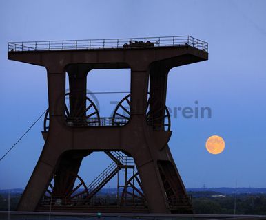 Das 55 Meter hohe Doppelbock-Fördergerüst ist das Wahrzeichen der Zeche Zollverein, der Stadt Essen und der gesamten Region: Die als Doppelstrebengerüst in Vollwandbauweise konstruierte Förderanlage ermöglichte eine doppelte Fördermechanik. Dadurch konnte die doppelte Menge an Förderwagen bzw. Fördergefäßen transportiert werden. Zollverein Schacht XII galt zu Betriebszeiten als die leistungsstärkste Zeche der Welt. 250 Stufen führen auf die oberste Plattform des Gerüstes, deren Seilscheiben sich auch heute noch manchmal drehen: Der Schacht wird von der RAG AG für die zentrale Wasserhaltung genutzt.

Areal A [Schacht XII], Fördergerüst [A1]