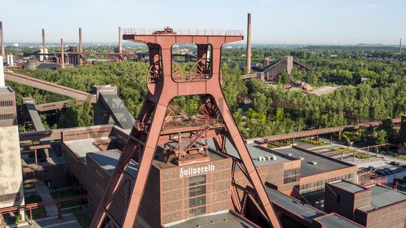 Das 55 Meter hohe Doppelbock-Fördergerüst ist das Wahrzeichen der Zeche Zollverein, der Stadt Essen und der gesamten Region: Die als Doppelstrebengerüst in Vollwandbauweise konstruierte Förderanlage ermöglichte eine doppelte Fördermechanik. Dadurch konnte die doppelte Menge an Förderwagen bzw. Fördergefäßen transportiert werden. Zollverein Schacht XII galt zu Betriebszeiten als die leistungsstärkste Zeche der Welt. 250 Stufen führen auf die oberste Plattform des Gerüstes, deren Seilscheiben sich auch heute noch manchmal drehen: Der Schacht wird von der RAG AG für die zentrale Wasserhaltung genutzt.

Areal A [Schacht XII], Fördergerüst [A1]