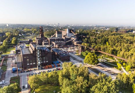 Die Geschichte Zollvereins beginnt in den Pioniertagen des heutigen Ruhrgebiets. Der erste Schacht wurde 1847 abgeteuft, d.h. in die Erde getrieben. Vier Jahre später wurde die erste Kohle gefördert. Im Laufe der Zeit entstanden vier weitere Schachtanlagen. Die letzte war die neue Zentralschachtanlage Zollverein XII, die ab 1932 die gesamte Zollverein-Kohle förderte. 

Noch heute besticht die symmetrische Anordnung der Gebäude auf zwei Blickachsen. Die komplett erhaltenen 20 Einzelgebäude bilden die technischen Arbeits- und Produktionsabläufe nach dem Prinzip „form follows function“ ab. Durchgestaltet bis in die Details der Lampen, Treppengeländer und Türgriffe, ist die Anlage ein komplett erhaltenes Gesamtkunstwerk. Die authentisch erhaltenen Anlagen repräsentieren exemplarisch die soziale, ökonomische, ästhetische und industrielle Geschichte des Kohle- und Stahlzeitalters. 

Trotz Rekordzahlen wie 12.000 Tagestonnen verwertbarer Steinkohle machte das Ende der Schwerindustrie auch vor Zollverein nicht Halt. Am 23. Dezember 1986 fuhr die letzte Schicht ein. An diesem Tag stand die Zeche bereits unter Denkmalschutz, 1990 begannen die Sanierungsarbeiten, seit 2001 sind Zeche und Kokerei Zollverein UNESCO-Welterbe. Mit dem Denkmalpfad ZOLLVEREIN®, dem Ruhr Museum und dem Red Dot Design Museum sind auf Schacht XII drei der beliebtesten Touristenziele der Region. Das Doppelbock-Fördergerüst der Schachtanlage ist heute Wahrzeichen für das gesamte Ruhrgebiet. 

Areal A [Schacht XII]